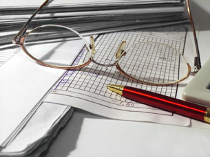 This photo shows a pair of eyeglasses, a pen, and accounting papers.