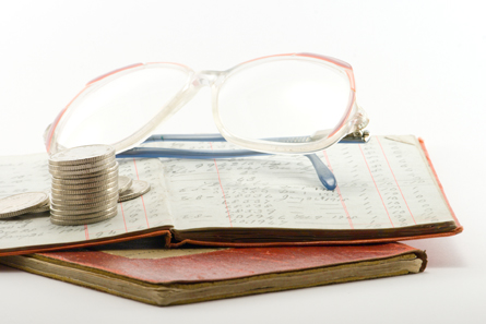 Two financial ledgers with a pair of spectacles and a pile of coins.
