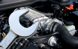 This picture shows a wrench with a car engine in the background.