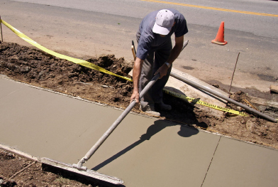 This photograph shows a worker smoothing concrete on a freshly poured sidewalk.