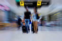 This photograph shows a man and a woman pulling suitcases in an airport.