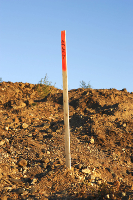 A photograph shows a survey stake in some excavated soil at a construction site.