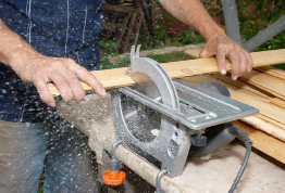 This photograph shows a carpenter using a saw to cut a board.