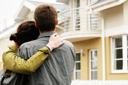 This photo shows a young couple hugging as they stand in front of a house.