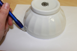 This photo shows a bowl inverted on a piece of paper. A pencil is tracing around the bowl.