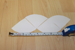 This photo shows quarters of a paper circle being arranged to form a parallelogram. A measuring tape lies along the bottom of the parallelogram.