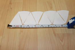 This photo shows eighths of a paper circle being arranged to form a parallelogram. A measuring tape lies along the bottom of the parallelogram.