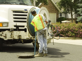This photograph shows a maintenance-hole cover and a man working over the uncovered space.