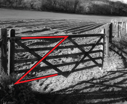 This is a photograph of a crossbraced wooden gate next to a ploughed field.