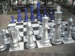 This photo shows two chess boards and pieces. One board is table top size. The other chess board is much larger, taking up space on a patio.