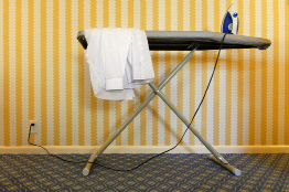 This picture shows and ironing board with a shirt on one end and an iron on the other. The two legs of the ironing board cross about one third of the distance from the horizontal ironing surface and the floor.