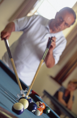 This is a photo of a man leaning over a pool table with a pool cue, and he is ready to take an awkward shot.