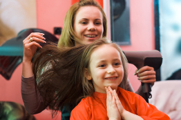 A hairstylist is drying the hair of a young customer.