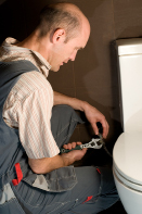 This is a photo of a plumber installing a toilet in a new construction.